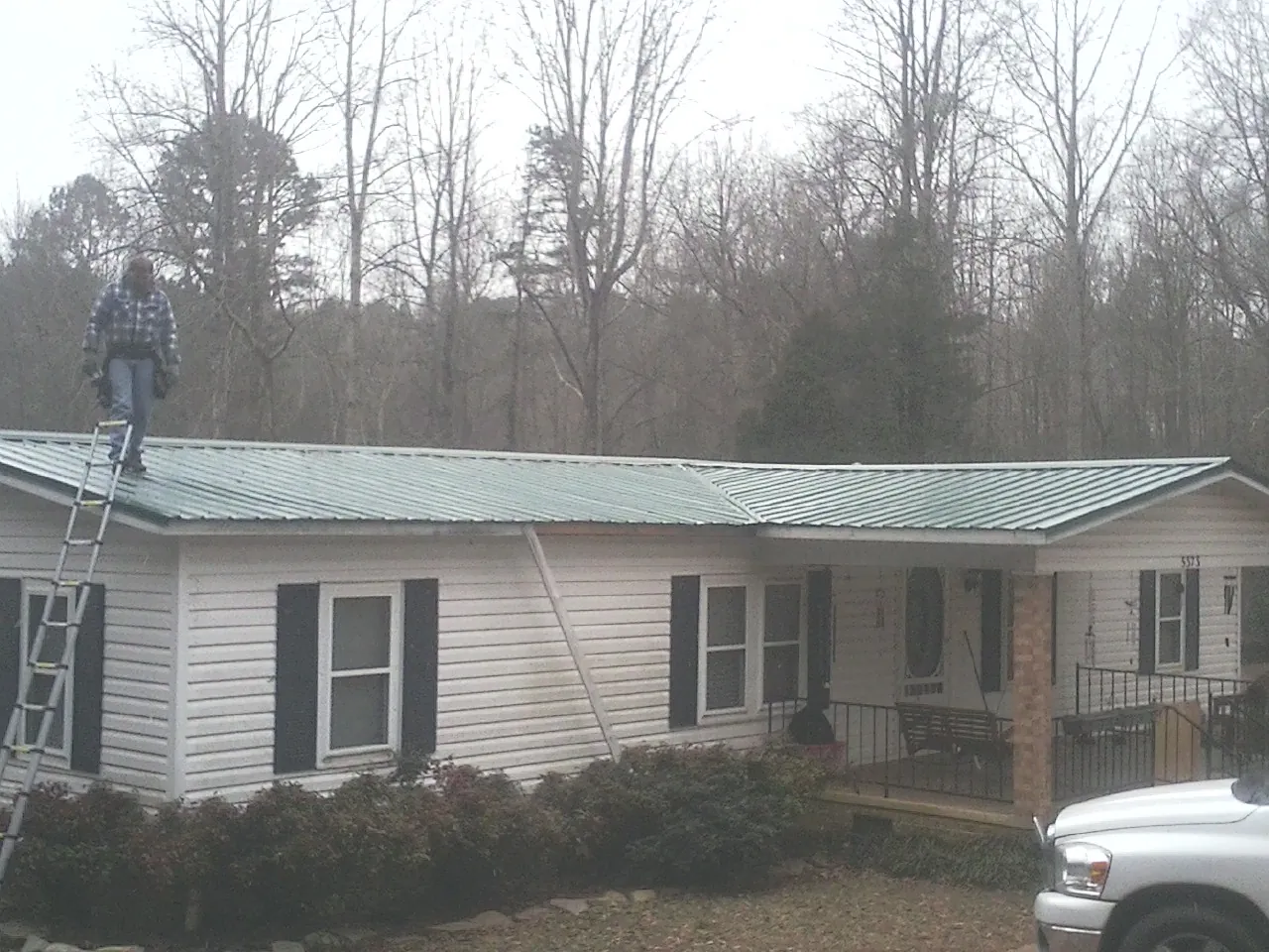 Worker on a ladder beside a new green metal roof on a ranch home in Ocean View